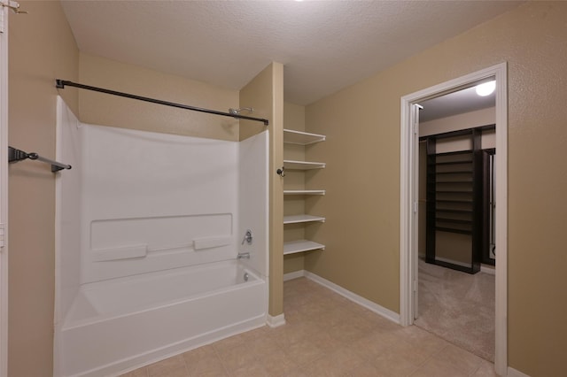 bathroom featuring a walk in closet, a textured ceiling, and baseboards