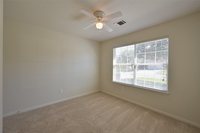 empty room featuring light carpet, ceiling fan, visible vents, and baseboards