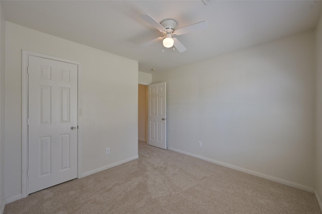 spare room featuring a ceiling fan, light colored carpet, and baseboards