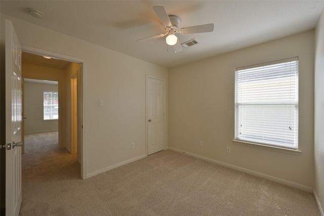 spare room with visible vents, ceiling fan, light carpet, and baseboards