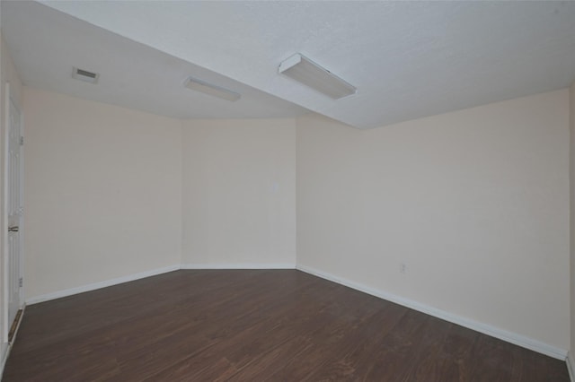 unfurnished room with visible vents, dark wood finished floors, and baseboards