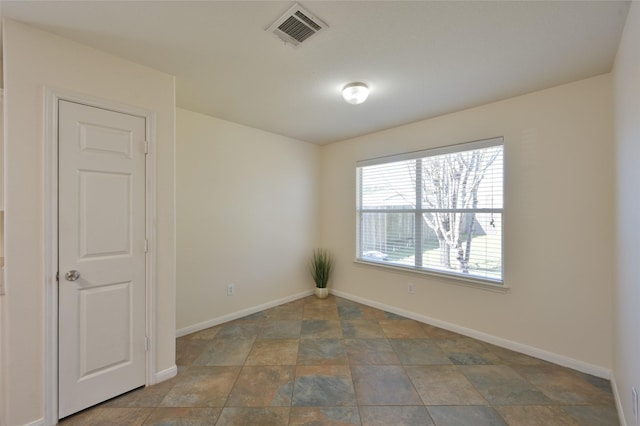 empty room with stone finish flooring, visible vents, and baseboards