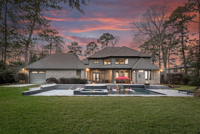 back of house at dusk featuring an attached garage, a patio area, and a lawn