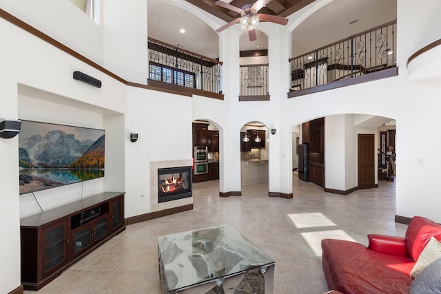 living area featuring ceiling fan, arched walkways, light tile patterned flooring, a multi sided fireplace, and baseboards