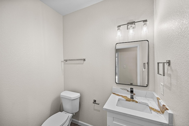 half bath with toilet, a textured wall, baseboards, and vanity