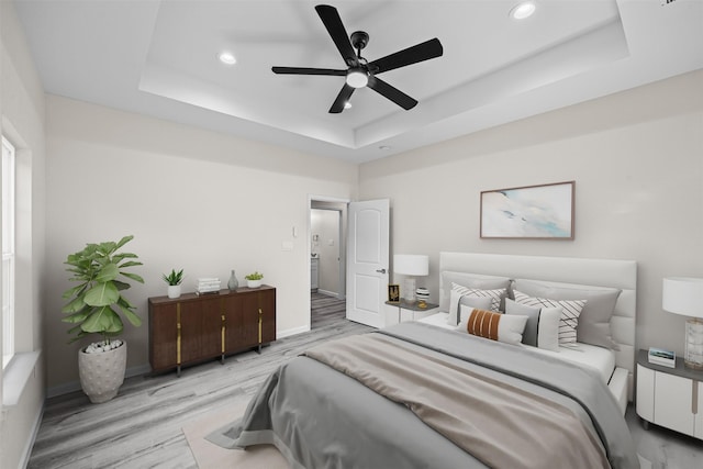 bedroom with a tray ceiling, recessed lighting, light wood-style floors, a ceiling fan, and baseboards