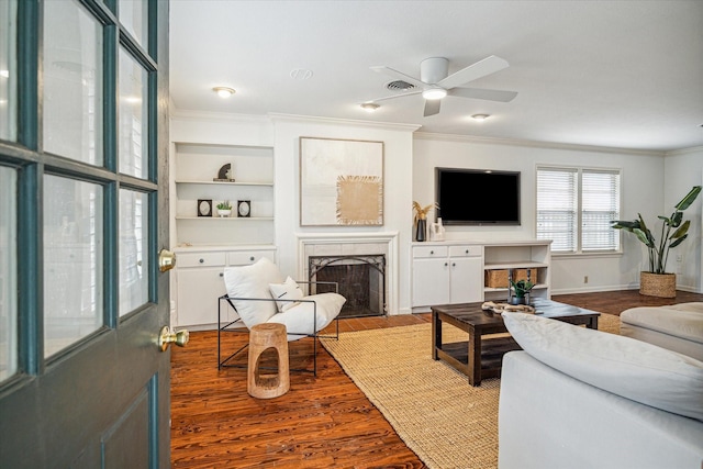 living room featuring built in features, crown molding, a high end fireplace, wood finished floors, and baseboards