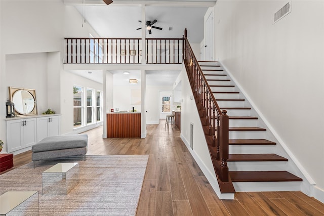 stairway featuring visible vents, a high ceiling, ceiling fan, wood finished floors, and baseboards