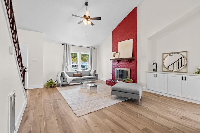 living room featuring light wood finished floors, visible vents, a ceiling fan, a brick fireplace, and high vaulted ceiling