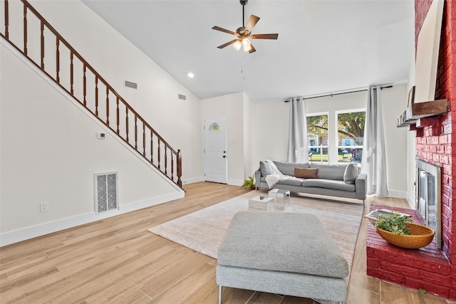 living area featuring visible vents, a fireplace, light wood-style flooring, and stairs