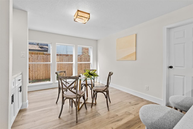 dining area with light wood-type flooring, baseboards, and a textured ceiling