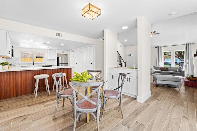 dining room featuring light wood-style floors, visible vents, plenty of natural light, and stairs