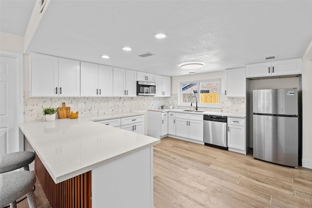 kitchen featuring white cabinets, a breakfast bar, a peninsula, stainless steel appliances, and light countertops