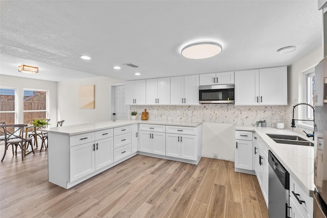 kitchen with a peninsula, stainless steel appliances, a sink, visible vents, and white cabinetry