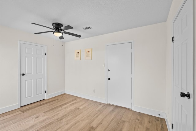 empty room featuring baseboards, light wood-style flooring, visible vents, and a textured ceiling