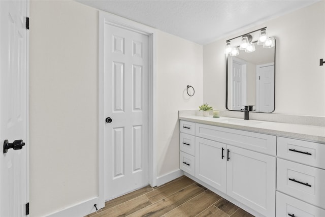 bathroom with a textured ceiling, wood finished floors, vanity, and baseboards