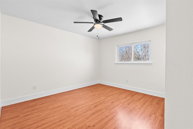 spare room with light wood-type flooring, a ceiling fan, and baseboards