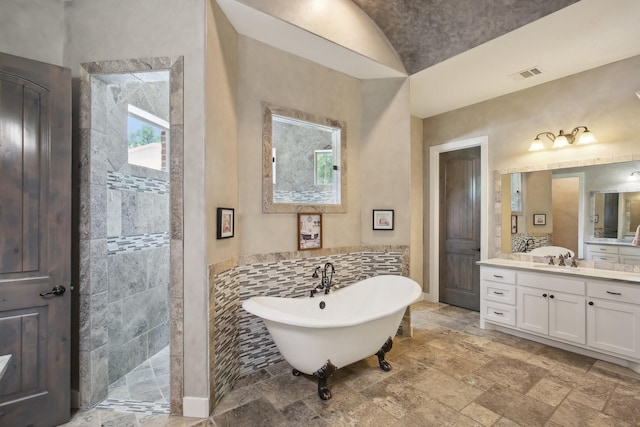 full bathroom with vanity, visible vents, a freestanding bath, a tile shower, and stone finish flooring