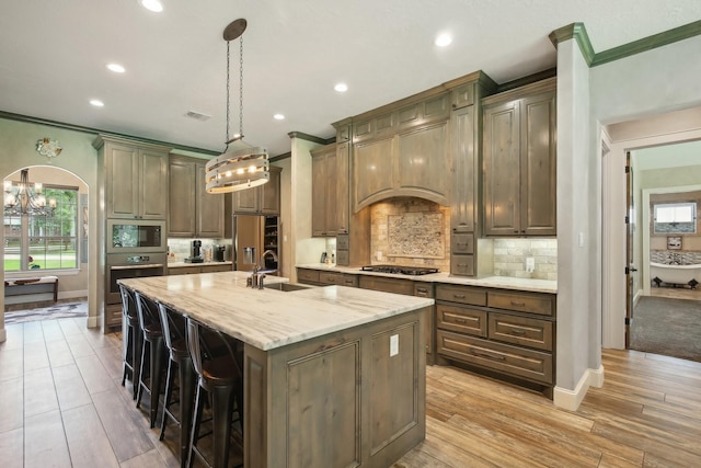 kitchen featuring arched walkways, decorative light fixtures, a sink, appliances with stainless steel finishes, and a center island with sink