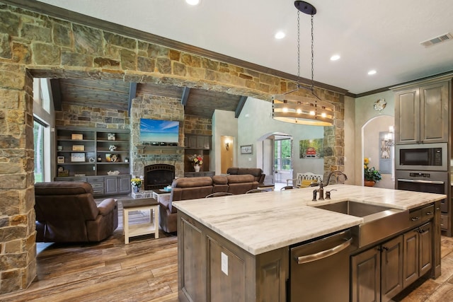 kitchen featuring arched walkways, stainless steel appliances, an island with sink, and a sink