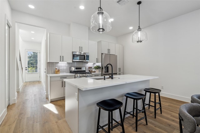 kitchen with decorative light fixtures, a center island with sink, light countertops, appliances with stainless steel finishes, and white cabinetry