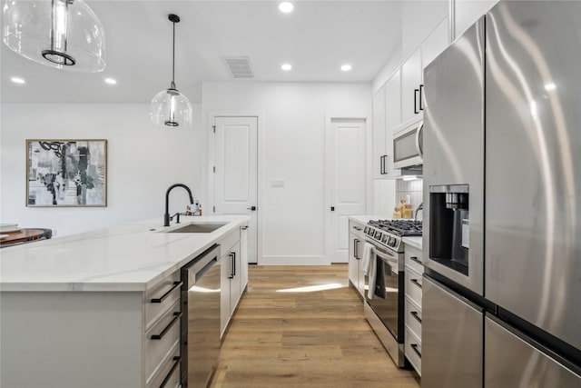 kitchen with an island with sink, appliances with stainless steel finishes, decorative light fixtures, white cabinetry, and a sink