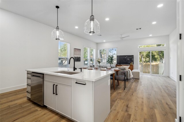 kitchen with decorative light fixtures, open floor plan, a kitchen island with sink, white cabinetry, and a sink