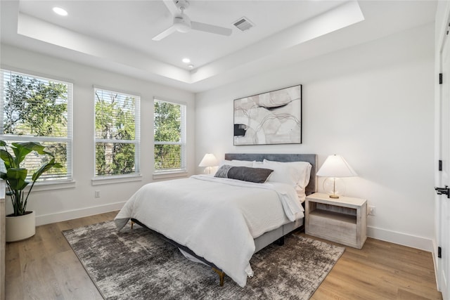 bedroom featuring light wood-type flooring, a raised ceiling, visible vents, and baseboards