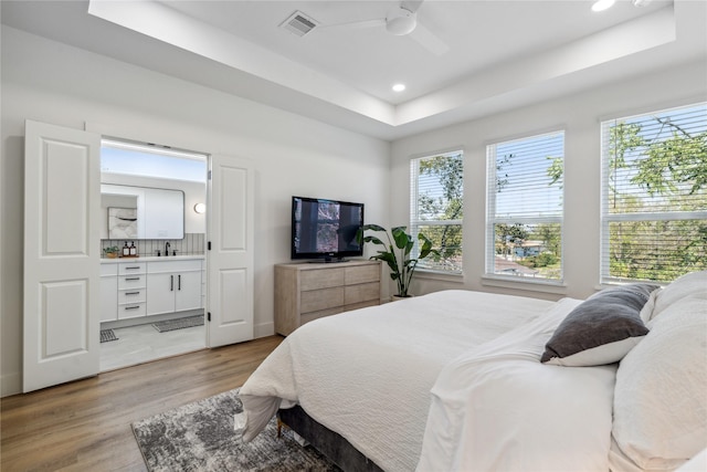 bedroom with light wood-style floors, a tray ceiling, multiple windows, and recessed lighting