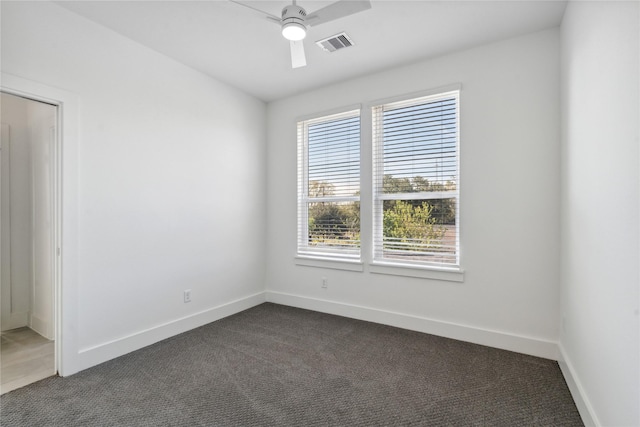 spare room with a ceiling fan, visible vents, dark carpet, and baseboards