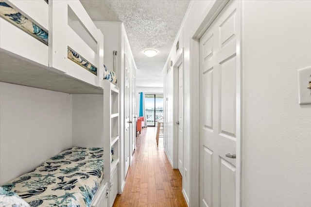 hallway with a textured ceiling, visible vents, and light wood-style flooring