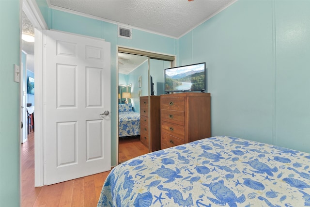 bedroom featuring a textured ceiling, ornamental molding, visible vents, and light wood-style floors