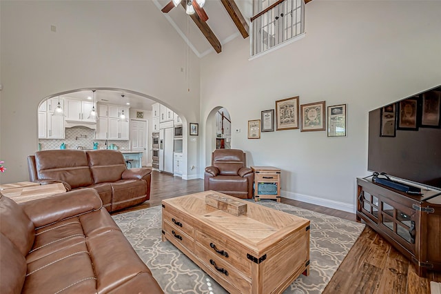 living area featuring arched walkways, ceiling fan, wood finished floors, beamed ceiling, and baseboards