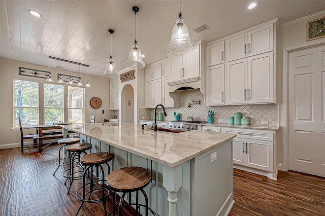 kitchen with arched walkways, dark wood-style flooring, a sink, white cabinets, and decorative backsplash