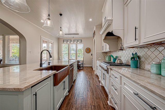 kitchen with arched walkways, stainless steel appliances, decorative backsplash, white cabinets, and a sink