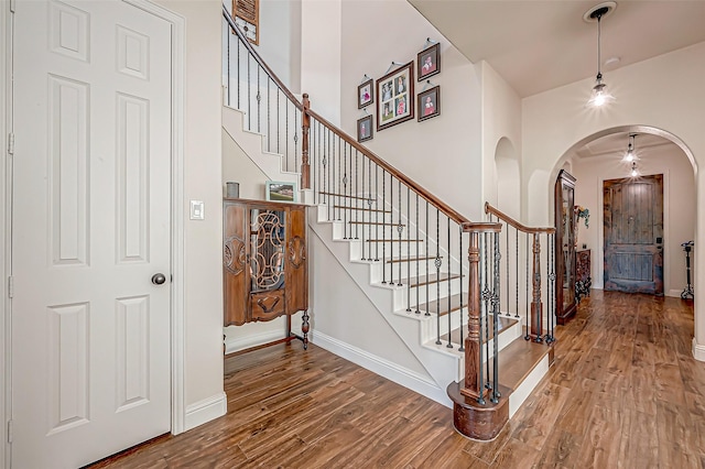 entrance foyer featuring baseboards, stairs, arched walkways, and wood finished floors