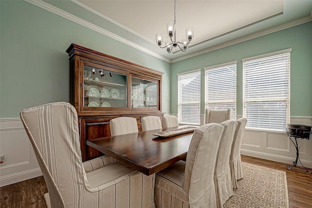 dining space featuring a decorative wall, wood finished floors, ornamental molding, wainscoting, and an inviting chandelier