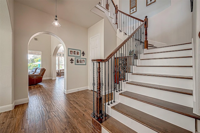 foyer featuring baseboards, arched walkways, a towering ceiling, stairway, and wood finished floors