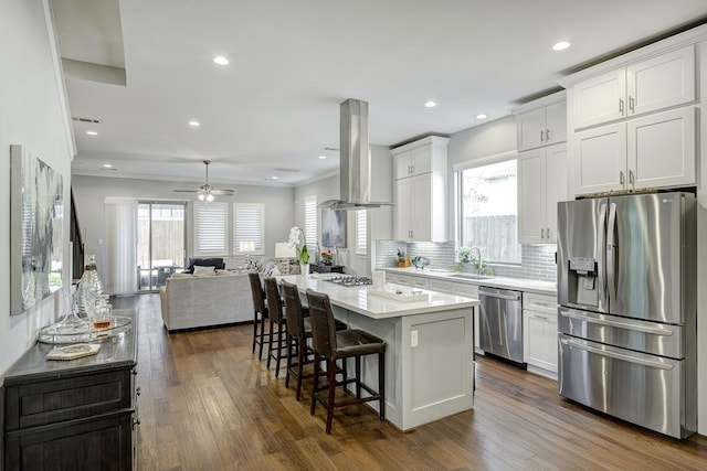 kitchen with island range hood, stainless steel appliances, a sink, white cabinetry, and open floor plan