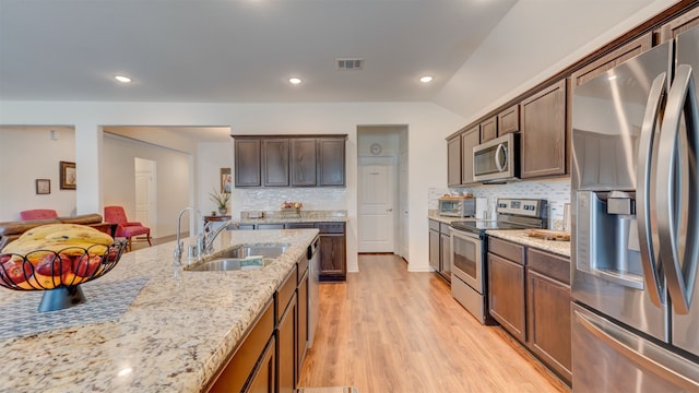 kitchen with light wood-style flooring, a sink, vaulted ceiling, appliances with stainless steel finishes, and light stone countertops