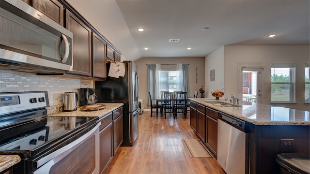 kitchen featuring a kitchen island with sink, stainless steel appliances, a sink, visible vents, and light stone countertops