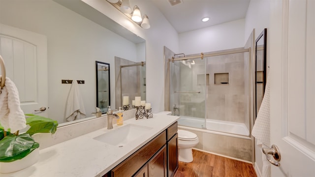 bathroom featuring vanity, combined bath / shower with glass door, wood finished floors, and toilet