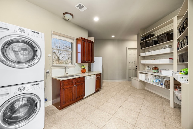 clothes washing area featuring laundry area, stacked washer / dryer, a sink, and baseboards