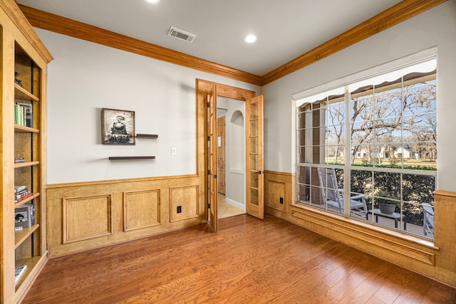 interior space featuring arched walkways, visible vents, wainscoting, ornamental molding, and wood finished floors