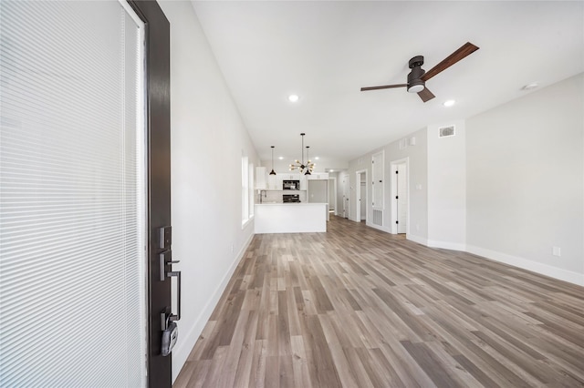 unfurnished living room featuring visible vents, baseboards, light wood-style flooring, ceiling fan with notable chandelier, and recessed lighting