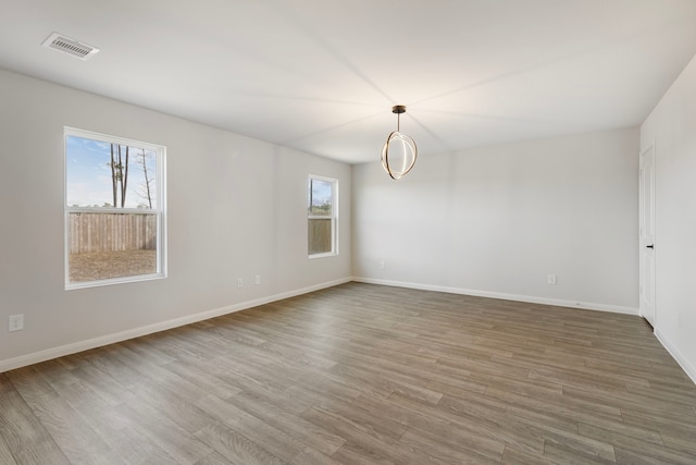 empty room with a wealth of natural light, visible vents, baseboards, and wood finished floors