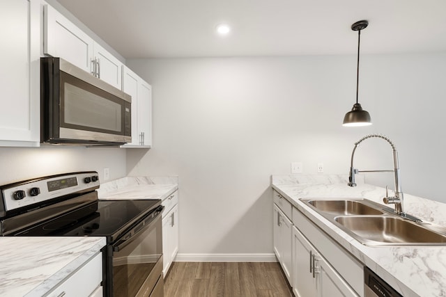 kitchen with appliances with stainless steel finishes, white cabinets, a sink, and decorative light fixtures