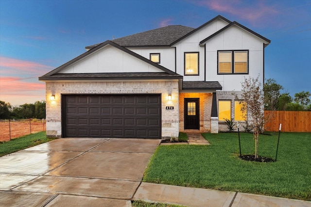 modern farmhouse featuring an attached garage, brick siding, fence, roof with shingles, and a lawn