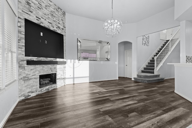 unfurnished living room featuring baseboards, wood finished floors, stairs, a fireplace, and a notable chandelier