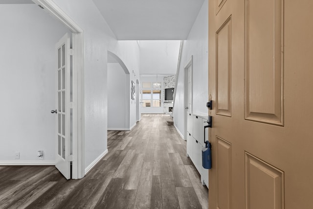 corridor featuring arched walkways, an inviting chandelier, wood finished floors, and baseboards